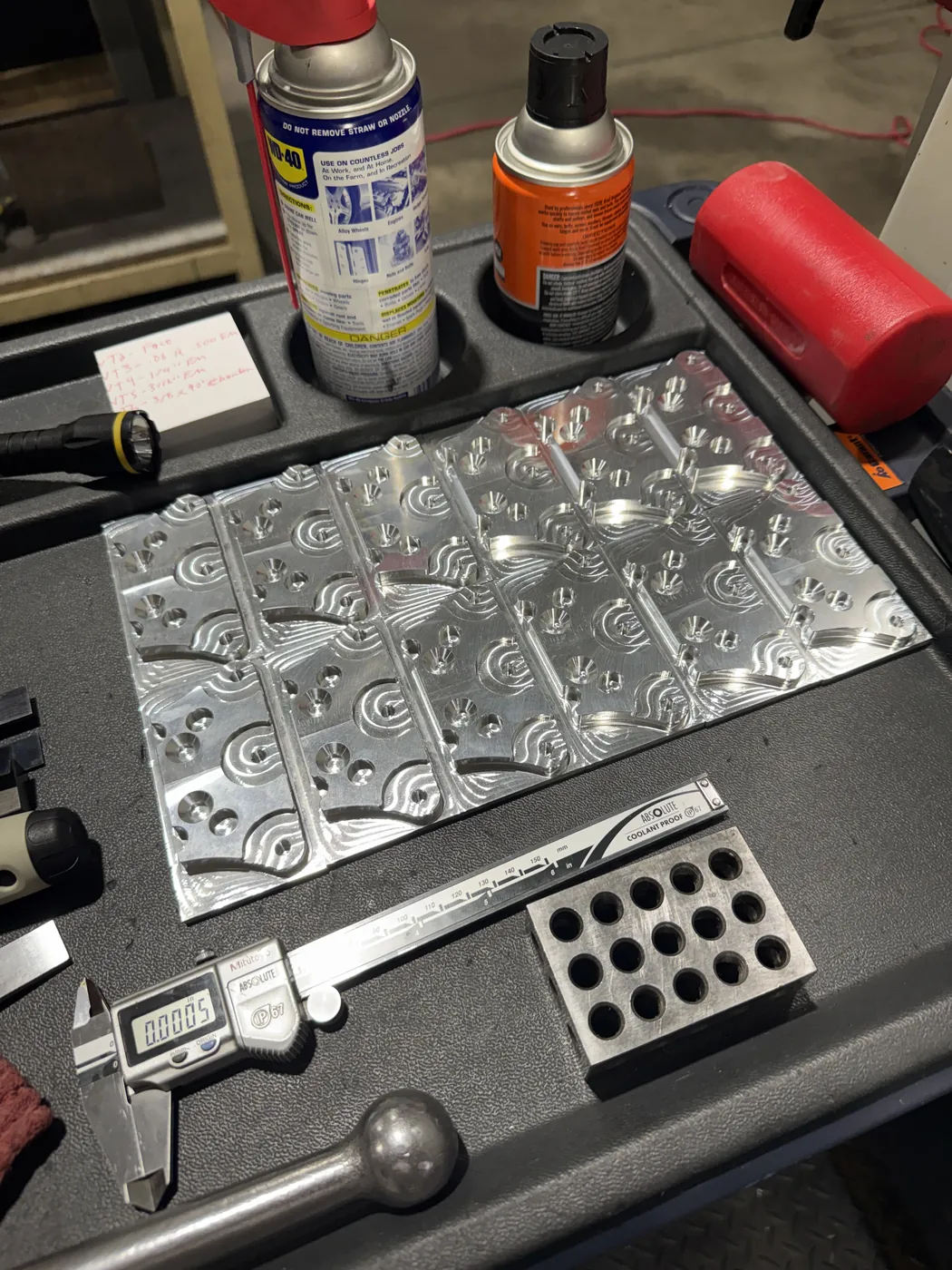 A batch of machined aluminum plates next to a digital caliper